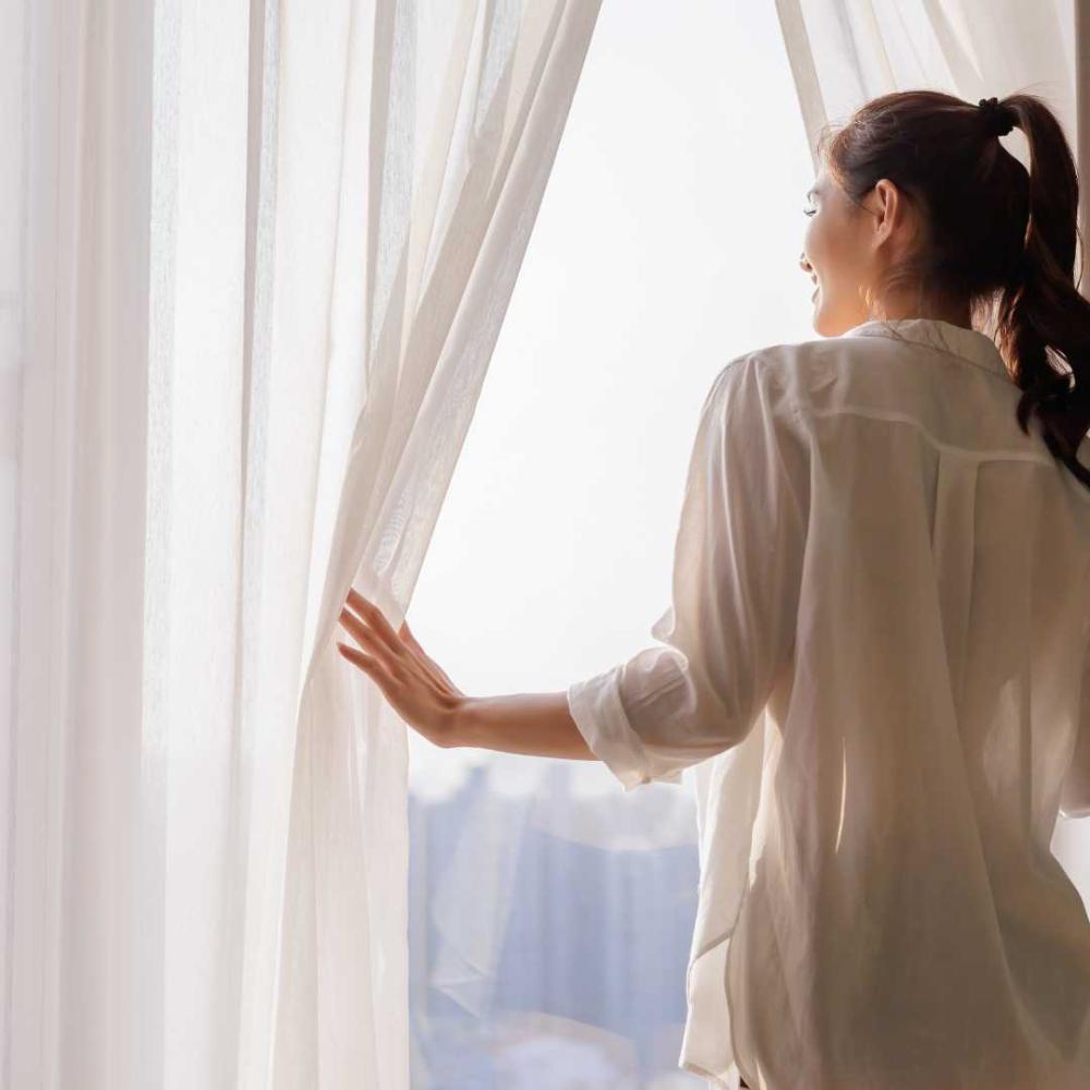 Person tittar ut från fönstret med mysiga gardiner i sovrum