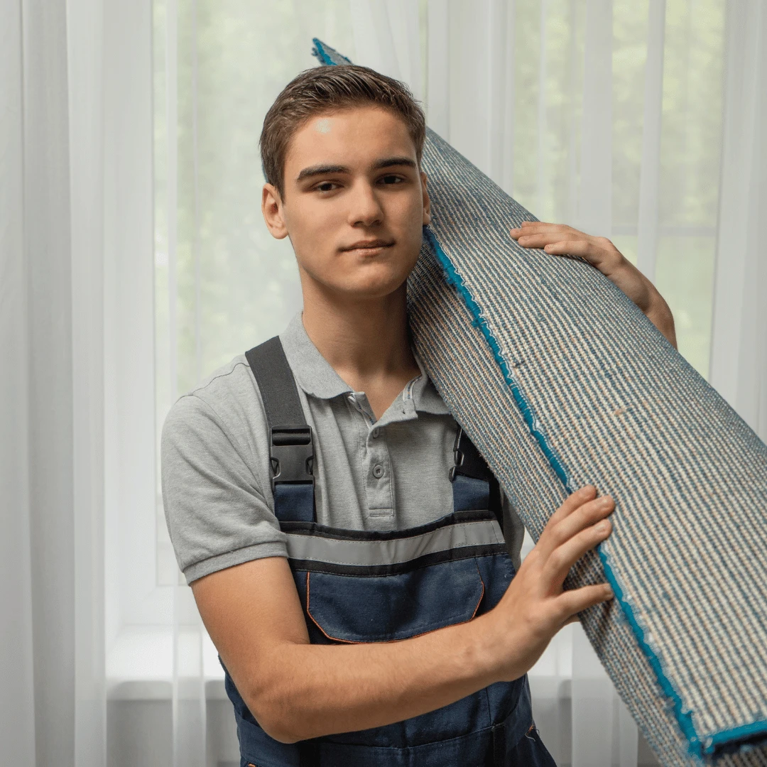 Professionell mattexpert med en ihoprullad matta över axeln och som gör sig redo inför en installation av glidskydd för matta.