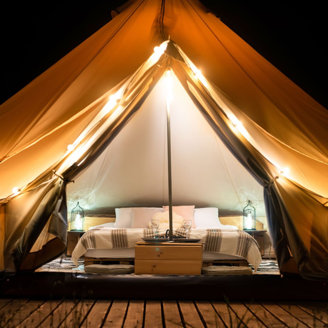 Ett tält med säng, tältmatta, sängbord och lampor.