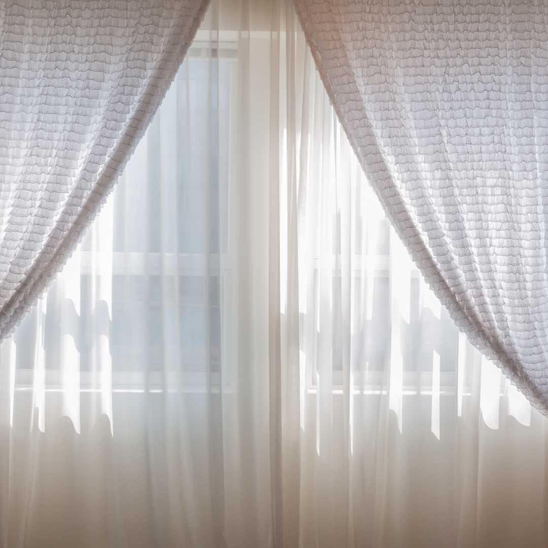 Nytvättade gardiner i krämvit färg hänger väldigt fint framför fönster.