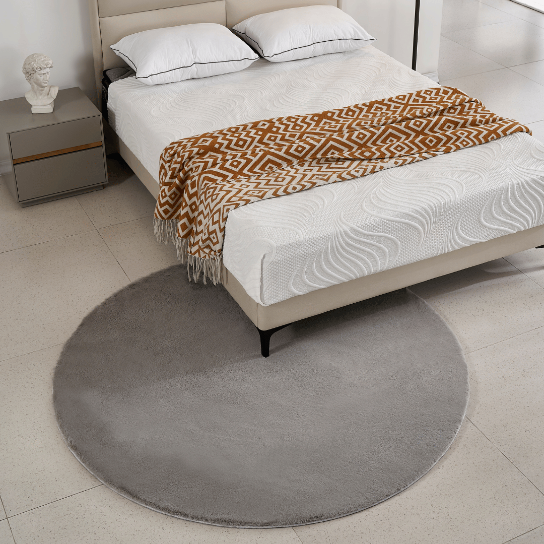 Rund anti-slip matta i grå färg bredvid säng i sovrum.