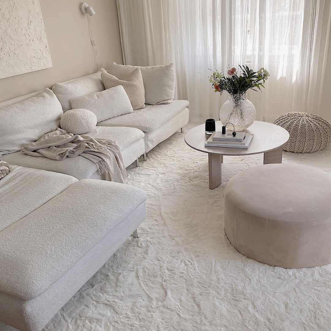 Vardagsrum i minimalistisk inredningsstil i neutral kräm och beige färgtoner. Mjuk matta, soffa och soffbord.