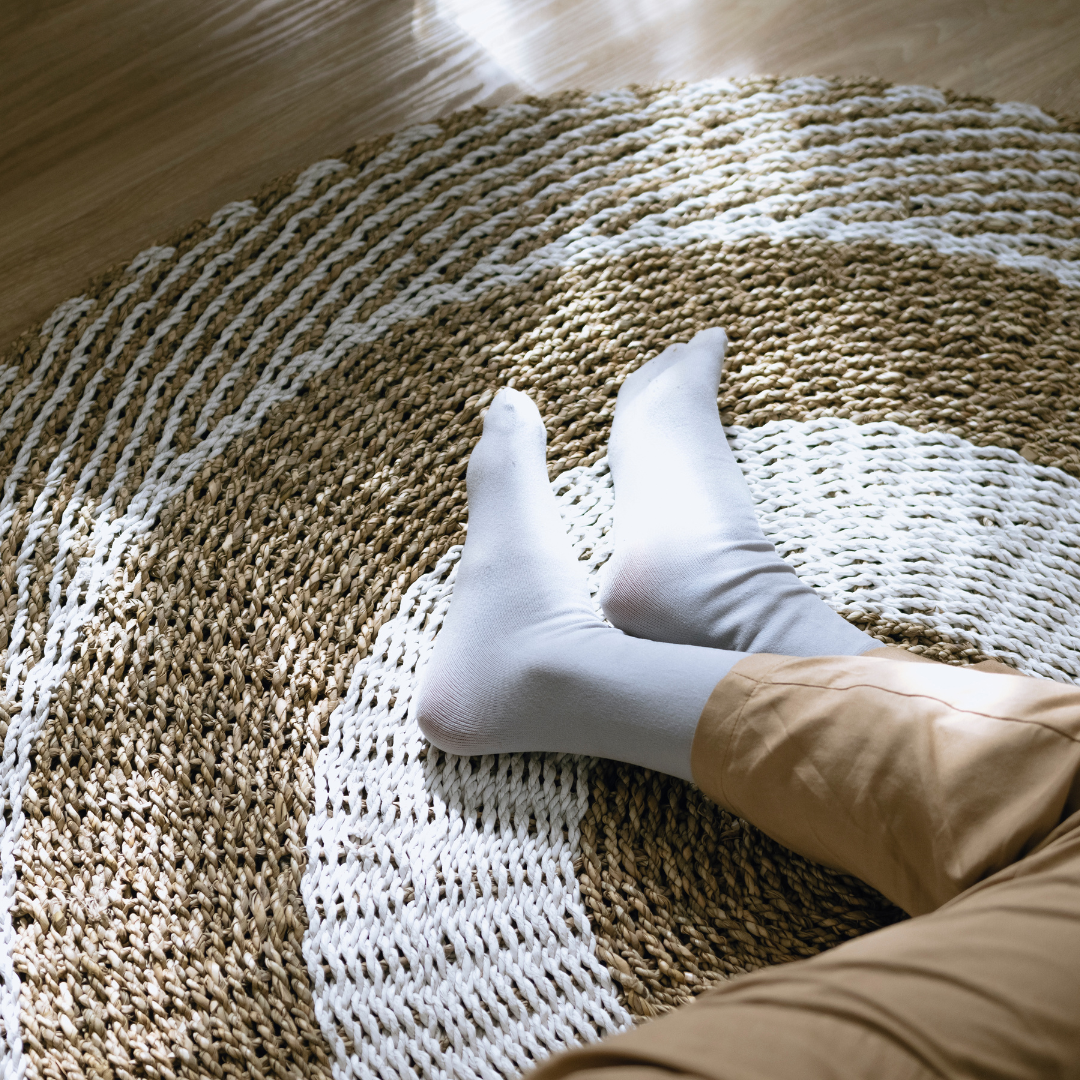 Person ligger på en matta av naturligt material. Man ser personens byxor och strumpor liggandes på soffan i en harmonisk atmosfär.