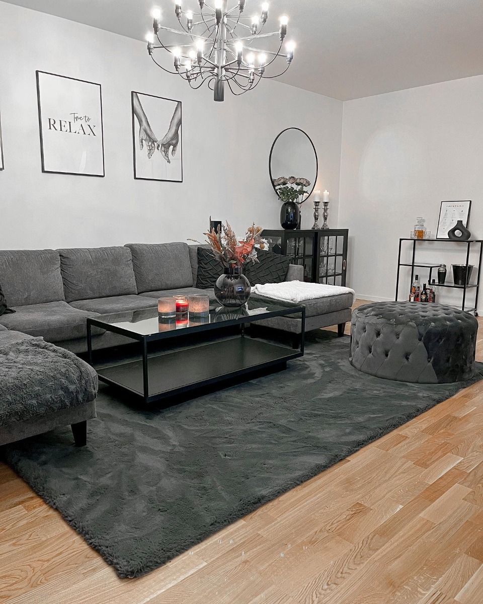 Stor svart matta under stor svart soffa skapar en enhetlig inredning som utstrålar elegans och stil.