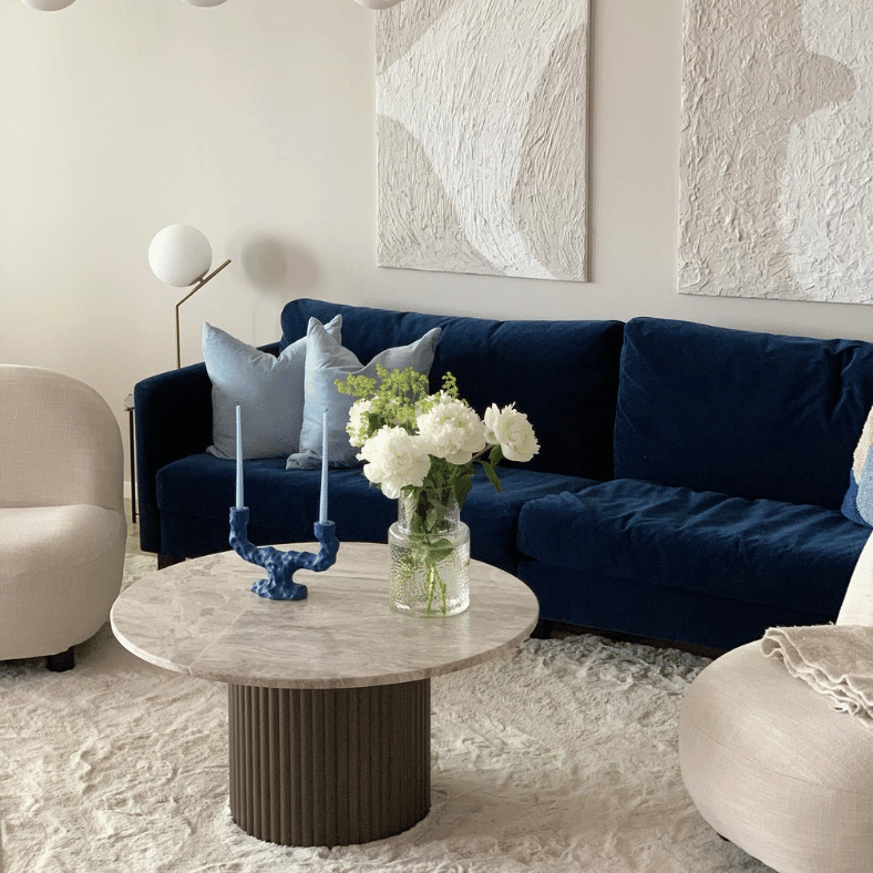 Runt soffbord med ljusbeige matta under och en blå soffa skapar elegans.