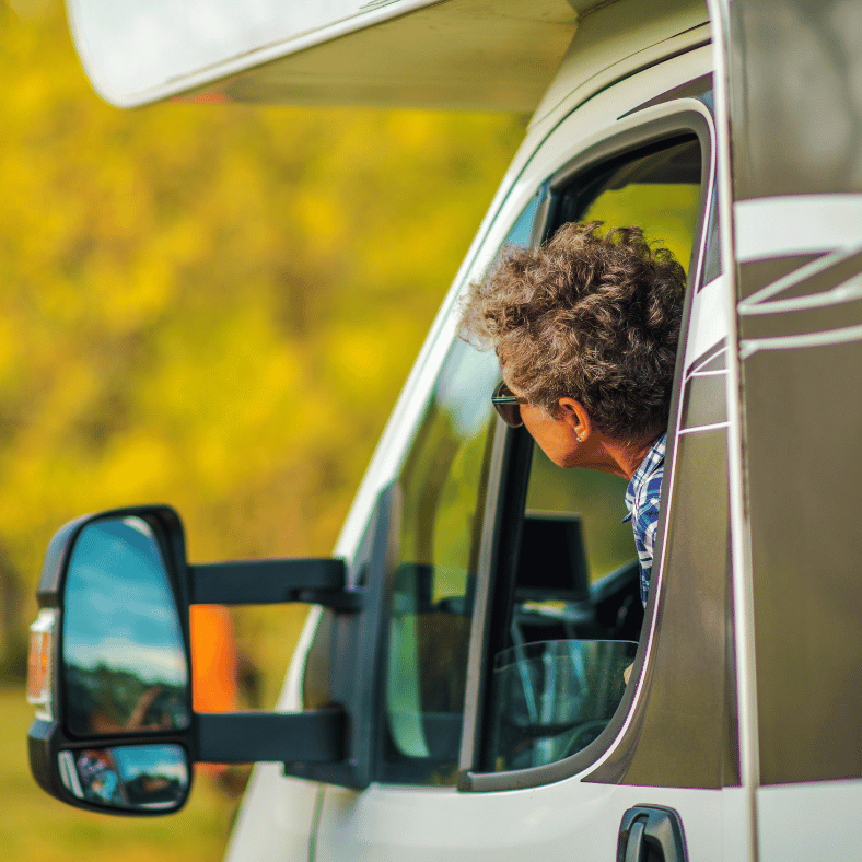 Person njuter av resan i husbilen genom att sticka ut huvudet ur fönstret och känna luften mot ansitket.