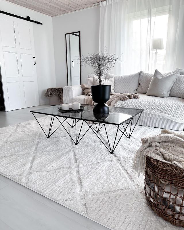 Ljusgrå soffa med en matta av samma färgton under. Utgör en snygg inredning i vardagsrummet.